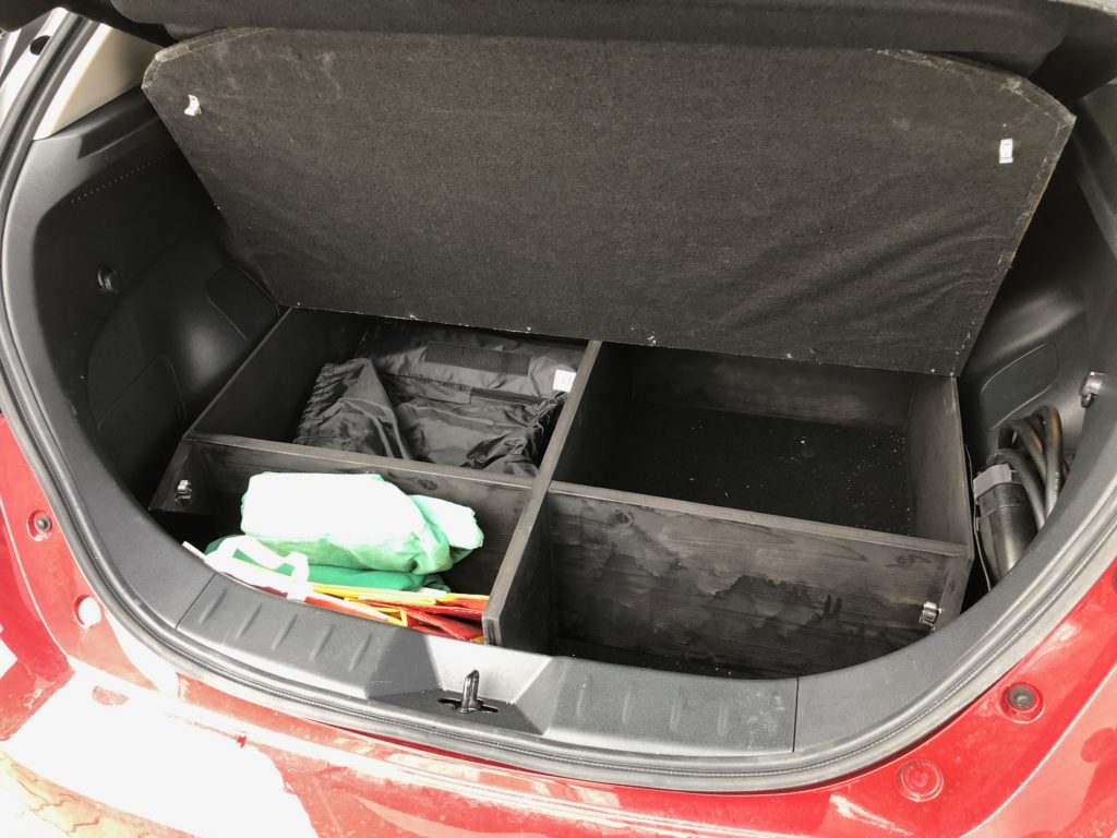 Offener Kofferraum eines roten Autos mit schwarzer Organizer-Box, grüner und weißer Tasche sowie orangefarbenem Zubehör