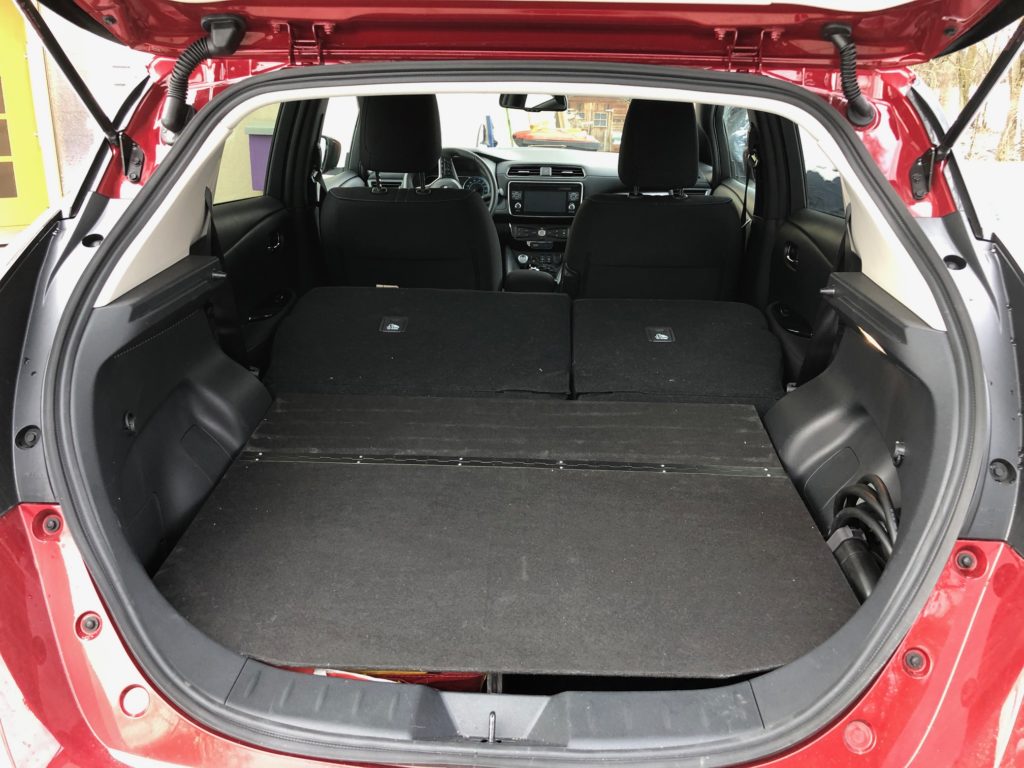 Rotes Auto mit offener Heckklappe, leerer schwarzer Kofferraum mit umgeklappten Rückseiten und Blick auf schwarze Sitze im Innenraum.